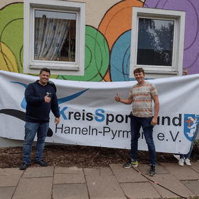 Zwei Männer stehen vor einem Banner mit dem Logo des KSB Hameln-Pyrmont und zeigen das Zeichen "Daumen hoch"