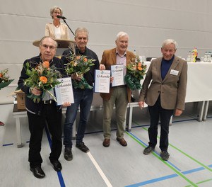 Vier Männer stehen nebeneinander, sie lächeln. Drei Männer links haben jeweils eine Ehrungsurkunde für ehrenamtliche Arbeit im Sportvereine und Blumen. Der Mann rechts hat die Urkunden übergeben.