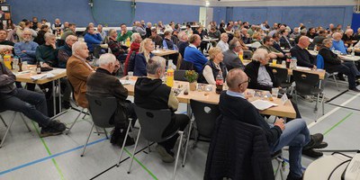 Zu sehen sind die Gäste des Kreissporttages 2023 des KSB Hameln-Pyrmont. Etwa 120 Personen sitzen an langen Tischreihen in einer Sporthalle mit Blick zum Podium.
